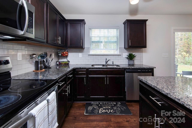 kitchen with appliances with stainless steel finishes, dark brown cabinets, light stone countertops, sink, and dark wood-type flooring