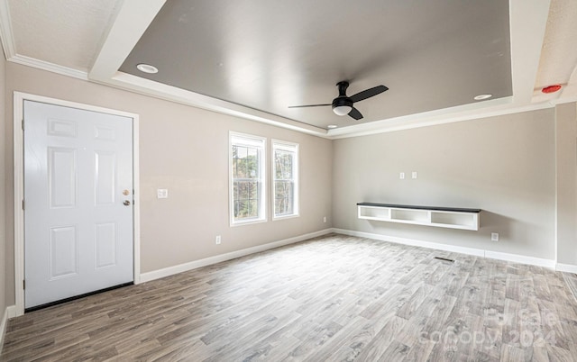 unfurnished living room with crown molding, hardwood / wood-style flooring, a tray ceiling, and ceiling fan