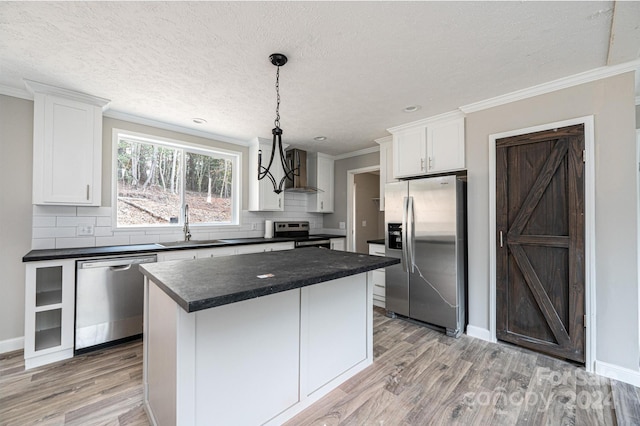 kitchen featuring hanging light fixtures, appliances with stainless steel finishes, white cabinetry, light wood-type flooring, and a center island