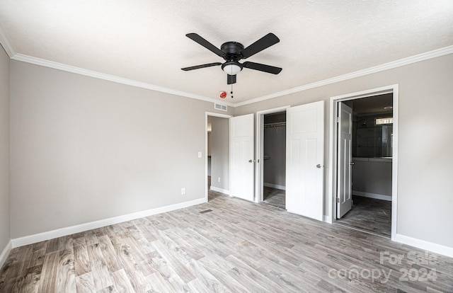 unfurnished bedroom featuring ceiling fan, a spacious closet, connected bathroom, light wood-type flooring, and ornamental molding