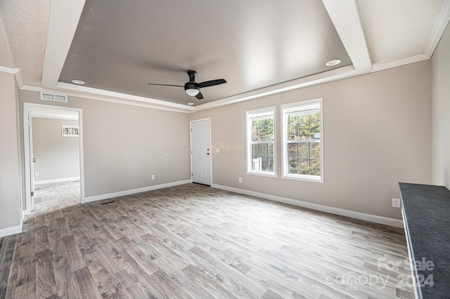 empty room with ceiling fan, ornamental molding, a tray ceiling, and light wood-type flooring