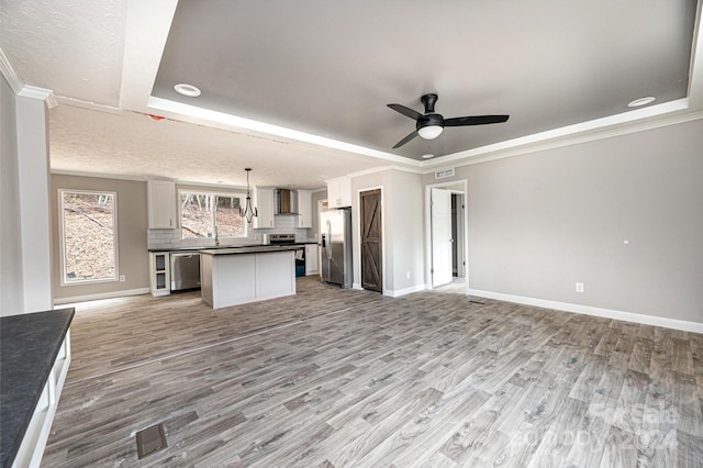 unfurnished living room with light hardwood / wood-style flooring, a tray ceiling, ornamental molding, a textured ceiling, and ceiling fan