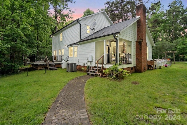 back house at dusk with a yard, a wooden deck, and central air condition unit