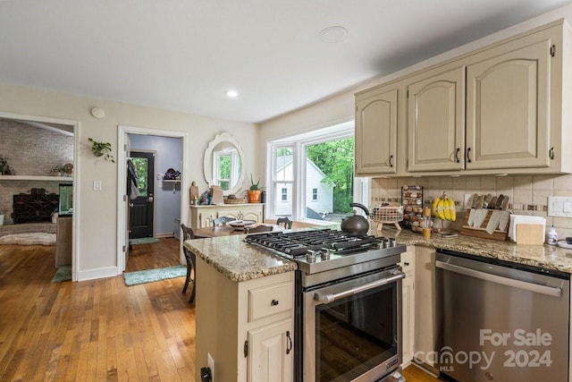 kitchen featuring backsplash, light wood-type flooring, light stone countertops, cream cabinetry, and stainless steel appliances