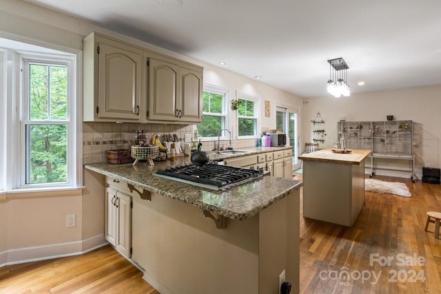 kitchen featuring a center island, sink, hanging light fixtures, light stone counters, and stainless steel gas stovetop