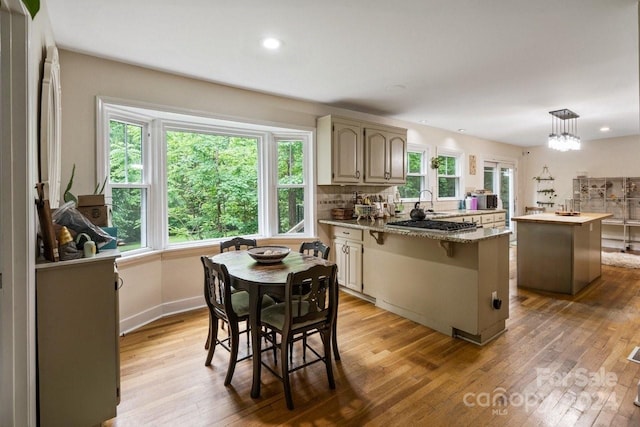 kitchen featuring a kitchen bar, light stone counters, light hardwood / wood-style flooring, a center island, and hanging light fixtures