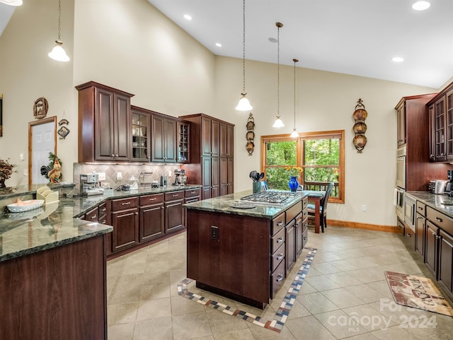 kitchen with high vaulted ceiling, tasteful backsplash, decorative light fixtures, and dark stone counters