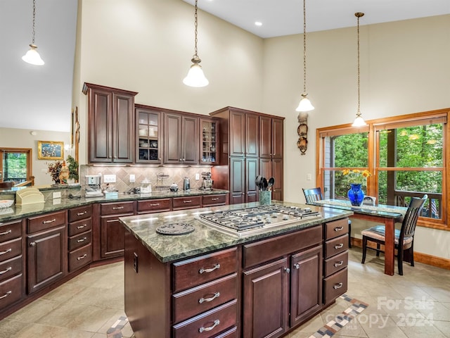 kitchen with a healthy amount of sunlight, tasteful backsplash, a towering ceiling, and light tile floors