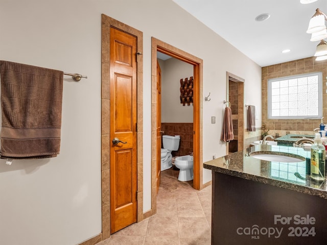 bathroom with tile walls, tile floors, toilet, vanity, and a bidet