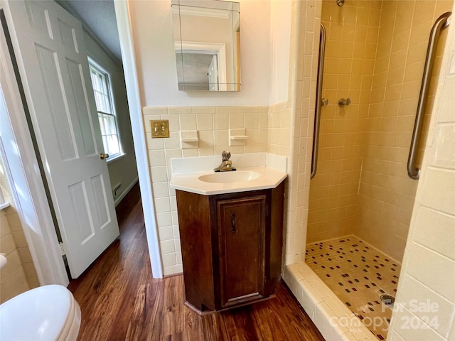 bathroom featuring hardwood / wood-style floors, toilet, a tile shower, tile walls, and vanity