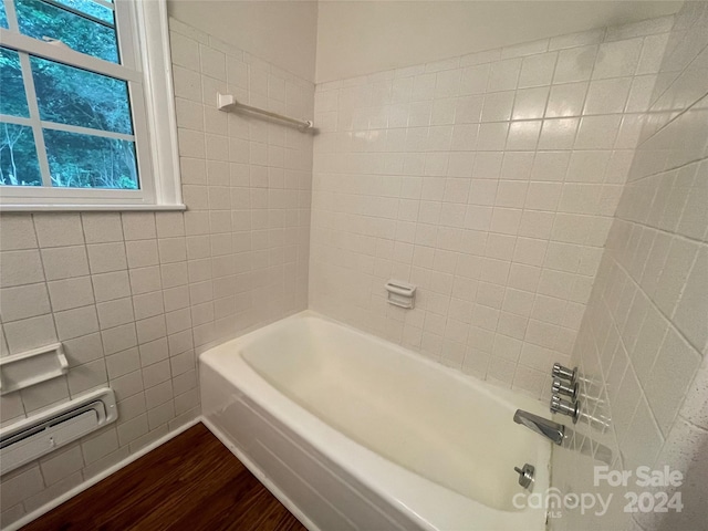 bathroom with hardwood / wood-style floors, tiled shower / bath, baseboard heating, and tile walls