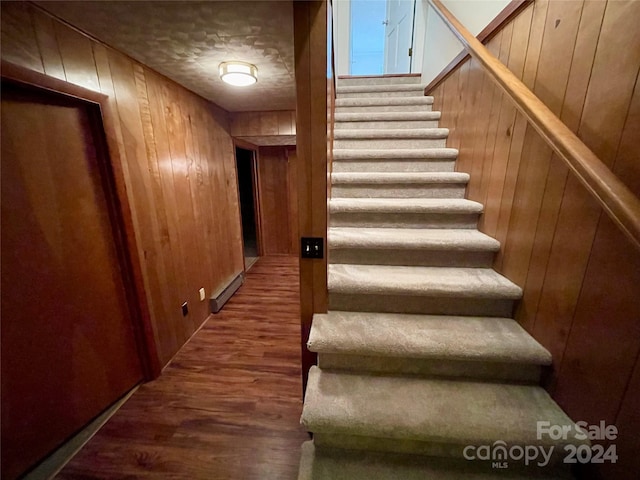 stairway featuring wood walls, wood-type flooring, and a baseboard heating unit