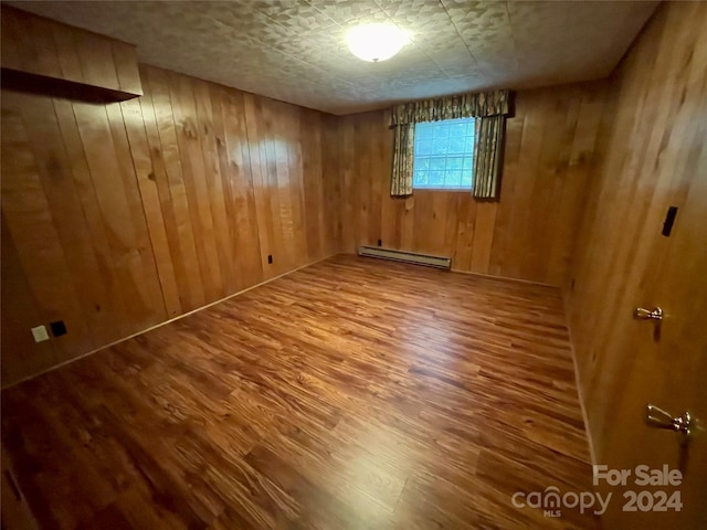 spare room with a baseboard heating unit, hardwood / wood-style flooring, and wood walls