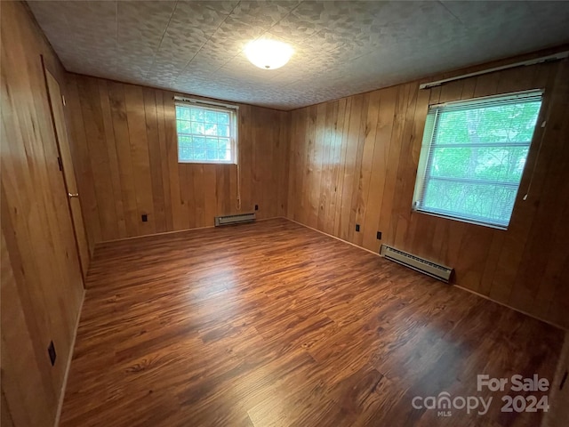 unfurnished room with a baseboard heating unit, wood walls, and hardwood / wood-style floors