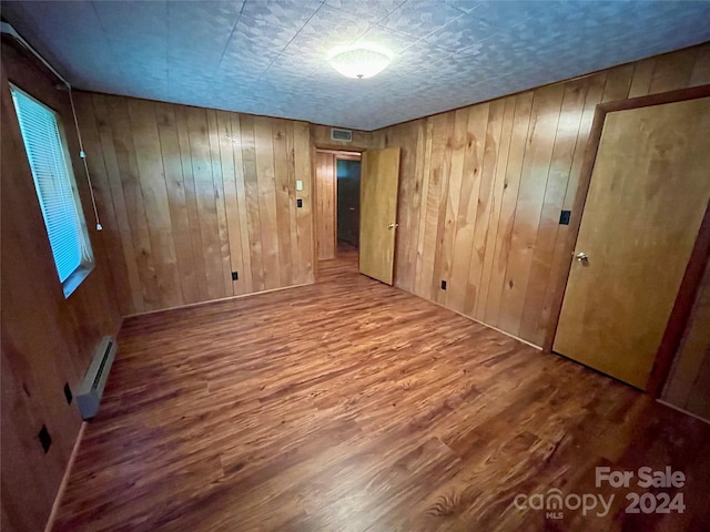 spare room with hardwood / wood-style floors, a baseboard radiator, and wooden walls