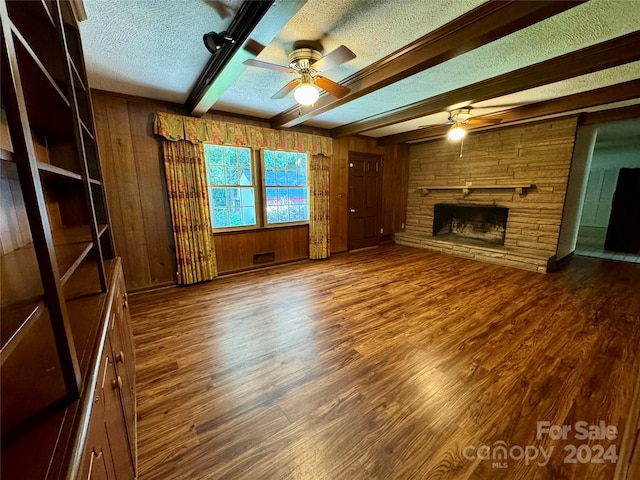 unfurnished living room featuring a fireplace, wooden walls, dark hardwood / wood-style flooring, beamed ceiling, and ceiling fan