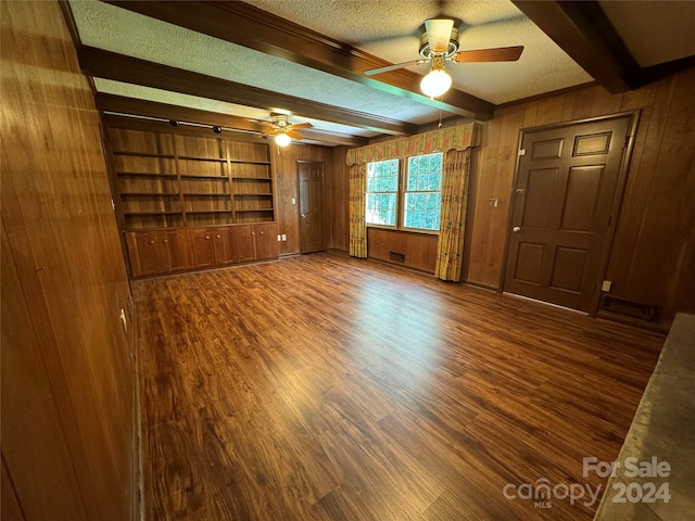 unfurnished living room with beamed ceiling, dark wood-type flooring, wood walls, ceiling fan, and a textured ceiling