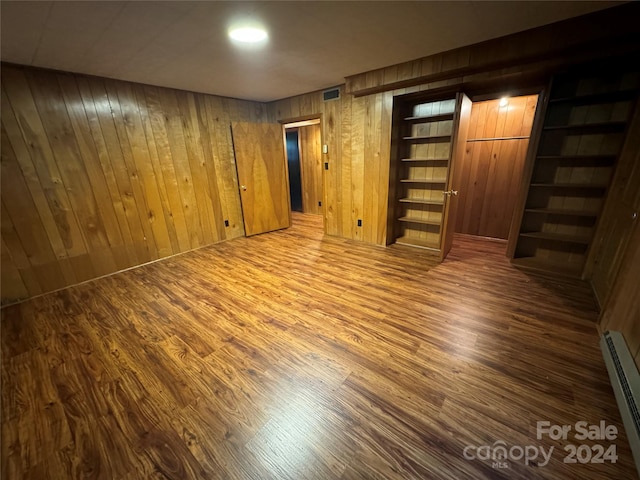 basement with a baseboard heating unit, dark wood-type flooring, and wooden walls