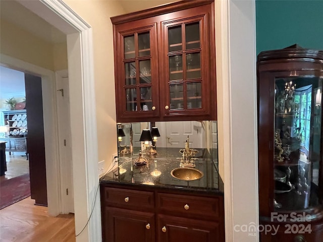 bar with dark stone countertops and light wood-type flooring