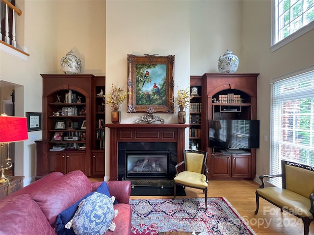 living room with a healthy amount of sunlight, light hardwood / wood-style flooring, and a towering ceiling