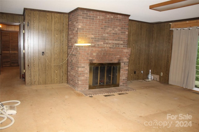 unfurnished living room with brick wall, wood walls, ornamental molding, and a brick fireplace