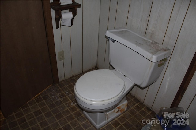 bathroom with tile floors, wooden walls, and toilet