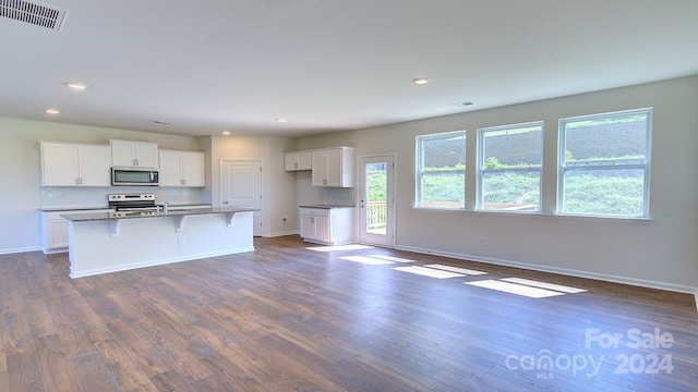 kitchen featuring a breakfast bar, a kitchen island with sink, white cabinets, appliances with stainless steel finishes, and dark hardwood / wood-style flooring