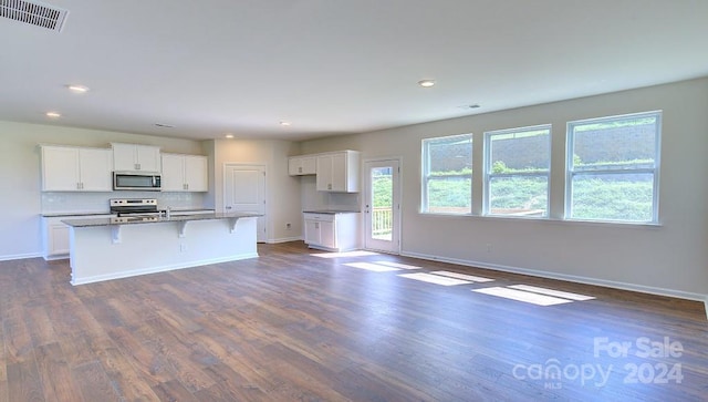 kitchen with appliances with stainless steel finishes, a kitchen breakfast bar, dark wood-type flooring, white cabinetry, and an island with sink