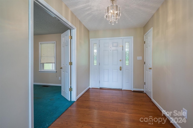 entryway featuring a healthy amount of sunlight, a notable chandelier, dark carpet, and a textured ceiling