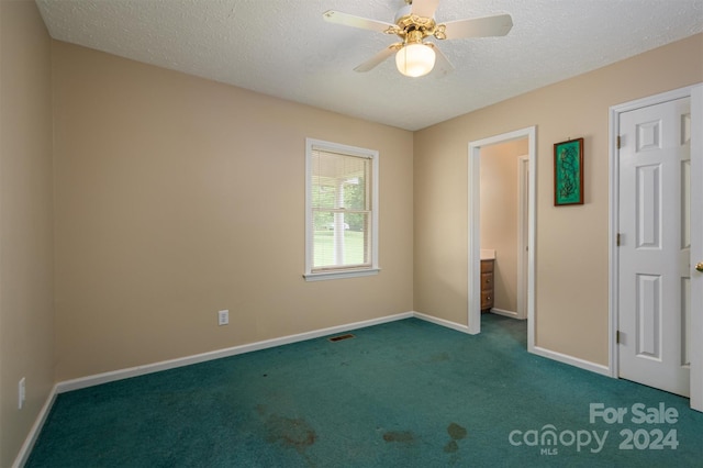 unfurnished bedroom with a textured ceiling, dark colored carpet, and ceiling fan