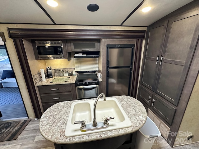 kitchen with light stone countertops, stainless steel appliances, light wood-type flooring, dark brown cabinetry, and sink