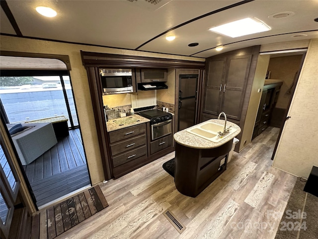 kitchen featuring light hardwood / wood-style floors, tasteful backsplash, dark brown cabinetry, stainless steel microwave, and light stone counters