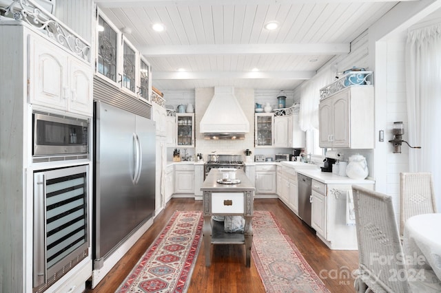 kitchen featuring built in appliances, beamed ceiling, beverage cooler, dark wood-type flooring, and custom range hood