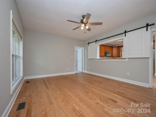 unfurnished living room featuring light hardwood / wood-style flooring, ceiling fan, a textured ceiling, and a barn door