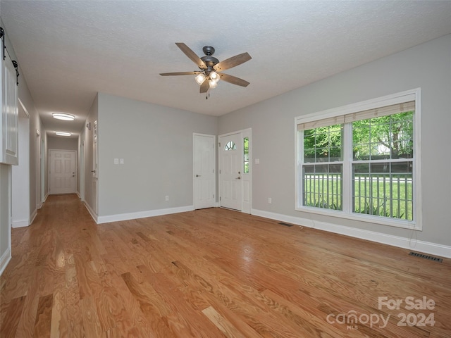 empty room with ceiling fan, a textured ceiling, and light wood-type flooring