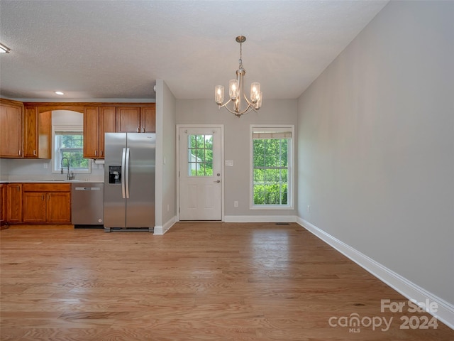 kitchen with an inviting chandelier, appliances with stainless steel finishes, decorative light fixtures, and light wood-type flooring