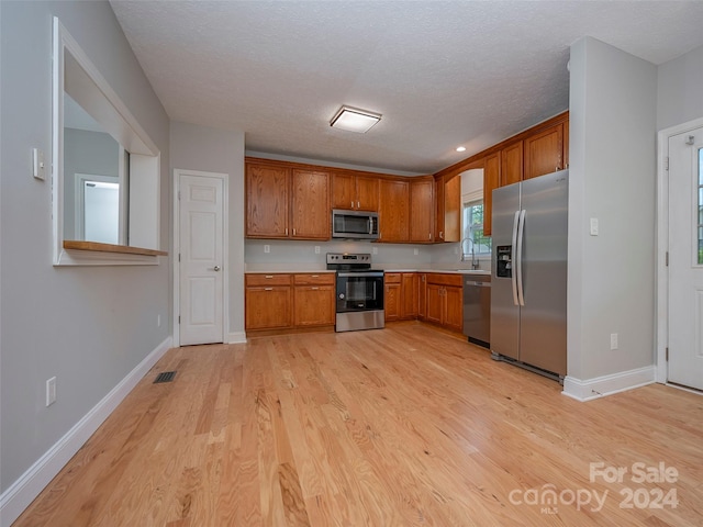 kitchen with appliances with stainless steel finishes, light hardwood / wood-style flooring, sink, and a textured ceiling