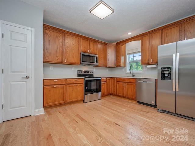 kitchen with appliances with stainless steel finishes, light hardwood / wood-style floors, a textured ceiling, and sink