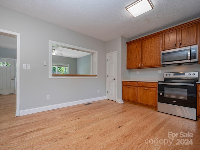 kitchen with ceiling fan, light hardwood / wood-style flooring, stainless steel appliances, and a textured ceiling