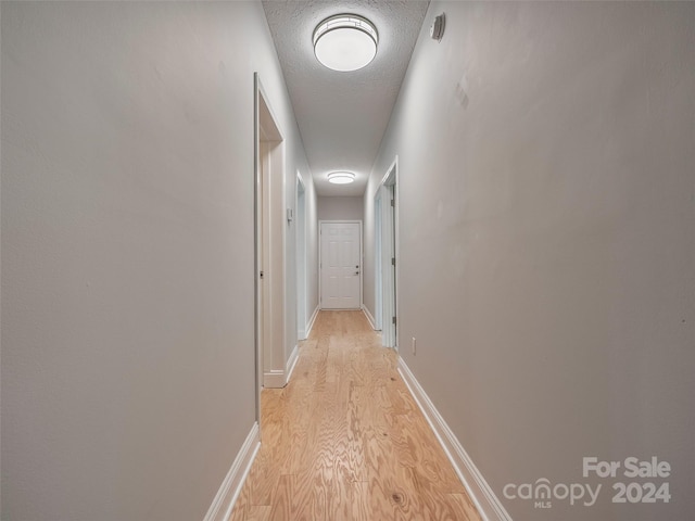 hall featuring light hardwood / wood-style floors and a textured ceiling