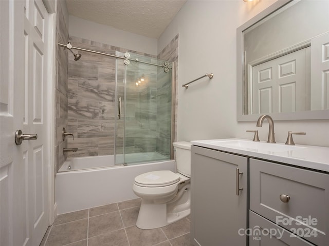 full bathroom featuring toilet, combined bath / shower with glass door, a textured ceiling, vanity, and tile floors