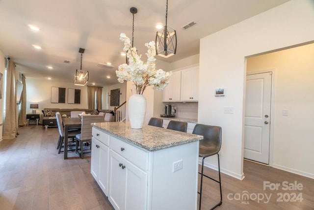 kitchen featuring a center island, a kitchen breakfast bar, hanging light fixtures, white cabinetry, and hardwood / wood-style flooring