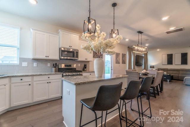 kitchen with a center island, white cabinets, backsplash, stainless steel appliances, and hardwood / wood-style flooring