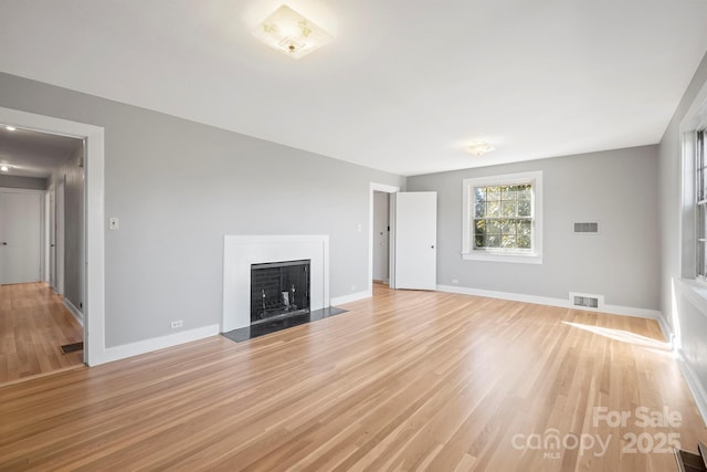 unfurnished living room with light wood-style flooring, a fireplace with flush hearth, and visible vents