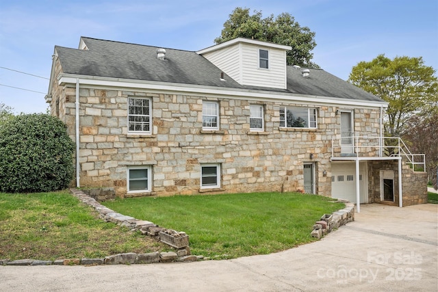 exterior space with driveway, a yard, an attached garage, a shingled roof, and stone siding