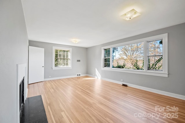 unfurnished living room featuring baseboards, a fireplace with flush hearth, visible vents, and light wood-style flooring