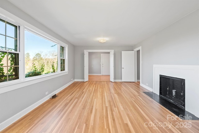 unfurnished living room featuring visible vents, baseboards, light wood-style floors, and a fireplace with flush hearth