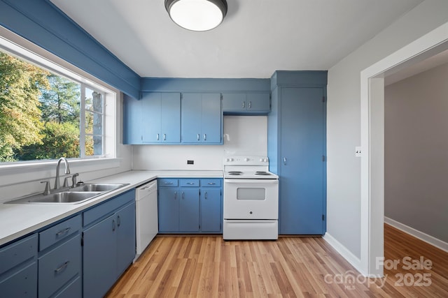 kitchen with white appliances, blue cabinetry, light countertops, and a sink