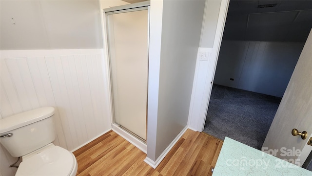 bathroom featuring a wainscoted wall, toilet, wood finished floors, and a shower stall