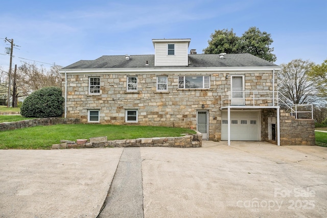 rear view of house with an attached garage, a lawn, a chimney, stone siding, and driveway